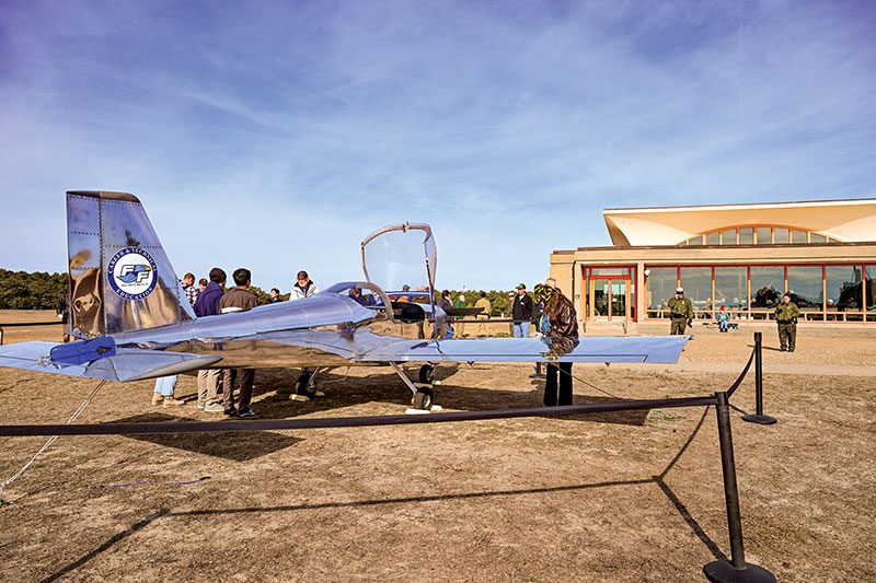With the Wright Brothers National Memorial looming in the background, a crowd of about a thousand people gathered Dec. 17, 2025 to both celebrate the anniversary of the Wright Brothers’ first flight in 1903 as well as the completion of a plane built by First Flight High School students on the same spot 122 years later. The plane will be ready for its first test flight in early 2026. Photo by Wes Snyder.